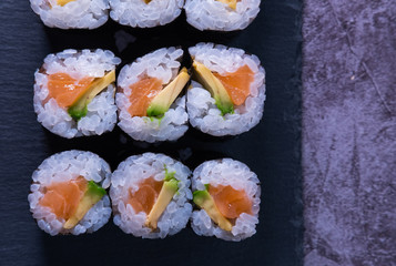 Salmon and avocado makis on slate purple and concrete background. Japanese food. Top view.