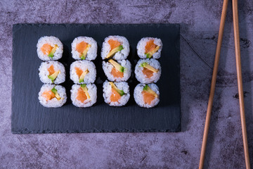 Salmon and avocado sushi maki rolls on a slate plate and chospsticks. Japanese cuisine. Top view.