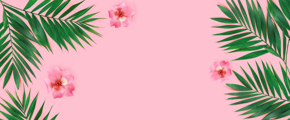 Creative flat lay top view of green tropical palm leaves with flowers  on pink paper background.