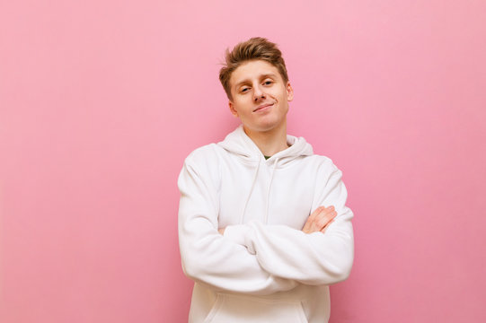 Portrait handsome blond boy in white casual clothes isolated on a pink background, looks into the camera and smiles.Young man in light hoodie posing at camera on pink background with smile on face