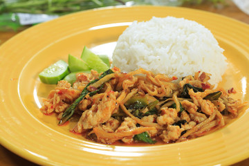 Rice topped with stir-fried bamboo shoots, minced pork, fried egg and cucumber on a yellow plate on a wooden table.