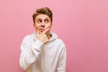 Funny young man isolated on pink background, looks away at copy space with pensive face. Pensive...