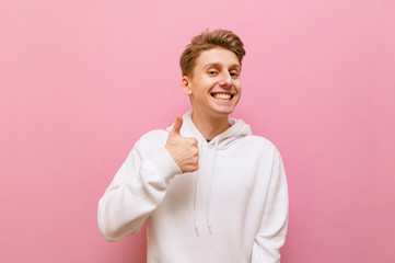 Happy young man in white casual clothes showing thumbs up, smiling and looking into the camera with...