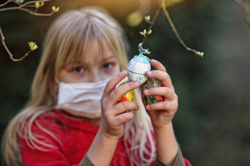young girl in a mask hangs an Easter egg on the tree
