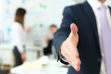 Businessman in suit and tie offering hand to shake to visitor closeup