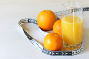 glass with orange juice and orange fruits with a measuring tape on the table. healthy diet for weight loss