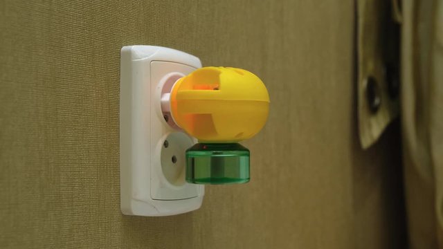 Male Hand Plug Electric Liquid Mosquito Repeller Into Electic Outlet on a Wall in a room. Camera moving, dolly shoot.