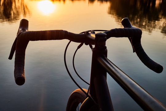 bicycle near lake, steering wheel over water on sunset background ,gravel bike close up - Powered by Adobe