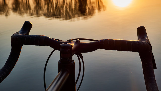bicycle near lake, steering wheel over water on sunset background ,gravel bike close up