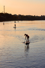 Silhouette of people paddle on standing up on paddle board (SUP) on Danube river at sunrise....