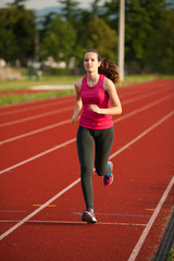 Beautiful young woman runner run on a track in early summer afternoon