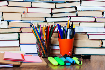 School stationery accessories - notebook, copybook stack with plastic holder pencils, pens, markers, paper clips, stickers, notepads, sharpener with stack of books education concept background.