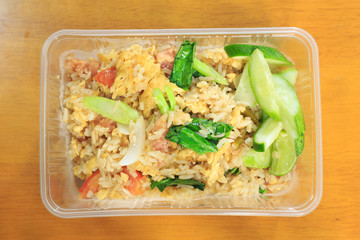 Fried rice with sour pork in a plastic wave box on a wooden table