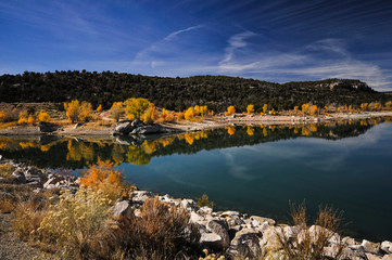 Fototapeta na wymiar Yellow trees in autumn next to a lake under blue skies during a sunny day