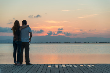 A sunset cloudy sky over a tranquil bay with a dock with a couple seen from behind