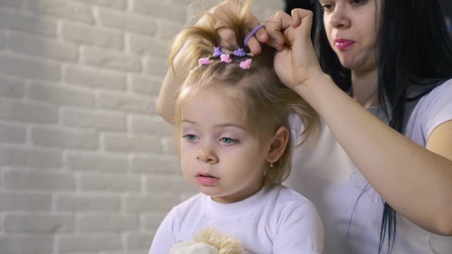 A caring young mother combs clean hair for her child. The girl makes a beautiful hairstyle for the baby.