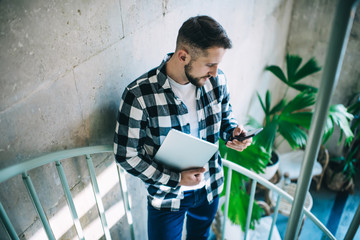 Positive male millennial checking notification about incoming mail on mobile phone spending time in...