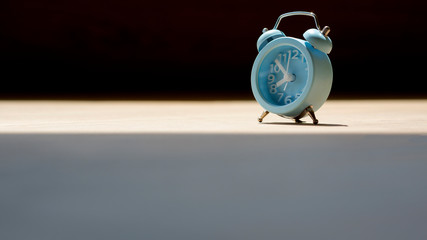 Sunlight and shadow on surface of little blue alarm table clock on wooden table in vintage tone...