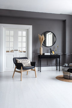 Modern living room interior with stucco molding on the walls with a Scandinavian-style armchair, console, mirror and coffee table.