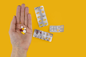 A pile of pills in hand on a yellow background. Dose of medication.