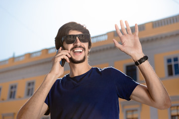 Young man in sunglasses smiling speaking on the mobile phone saying hello walking down the street