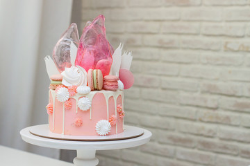 Modern pink cake with chocolate decor, caramel, french macaroons, meringues and waffle paper. White background
