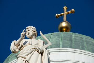 Fragment of Helsinki Cathedral , also knows as St Nicholas' Church, showing the statue of Apostle with the main dome with top cross at the background against the blue sky, shot at low angle