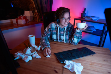Smiling woman with eyeglasses and headphones watching video on a computer and drinking coffee