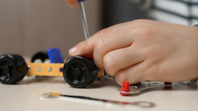 A small boy builds a car model from a metal construction kit, twisting the parts. Close-up of the child's hands.