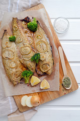 fresh tender baked mackerel with rings of chopped onion, broccoli and lemon on a dark wooden cutting board in baking paper. keto and flexitarian diet and healthy eating. with copy space
