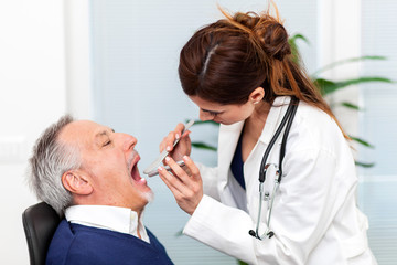 Female doctor visiting a patient by checking his throat