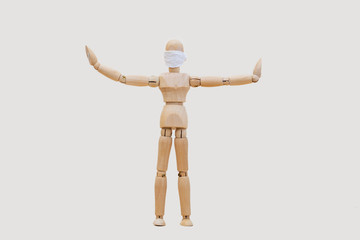 Wooden man mannequin in a protective medical mask holds his hands in different directions standing on a light gray background. Concept - keep your distance during quarantine.