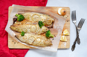 tender baked mackerel with rings of chopped onion, broccoli and lemon on a light background on a wooden cutting board in baking paper with a red napkin. keto and flexitritis diet and healthy eating.