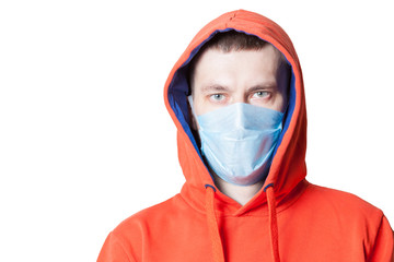 A man in an orange hoodie with a head-clad hood with a medical mask on his face during a coronavirus epidemic while defending himself against Covid-19 infection on a white isolated background.