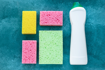 Kitchen sponges and antibacterial cleaner in bottle, disinfection concept. Housekeeping, housework. Colorful sponges for washing dishes and cleaning on green background.