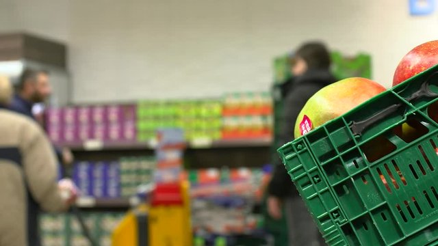 Tropical fruit mango in plastic green box in supermarket while customers passing by, close shot.