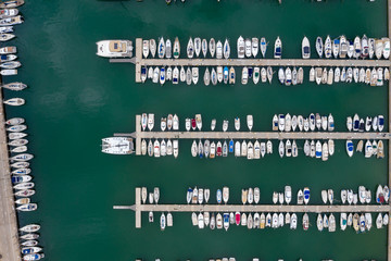 Aerial top-down photo of marina a dock basin with moorings and supplies for yachts and small boats showing the floating dock walkway supported by pontoons and the recreational motor boats