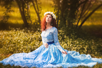 Portrait of an attractive woman with a rim of white flowers and in a blue magnificent dress sitting...