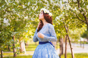 A beautiful woman in a blue puffy dress with a rim of white flowers on her head walks through the...