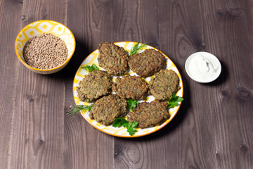 Lentil fritters in plate with sour cream on brown wooden background