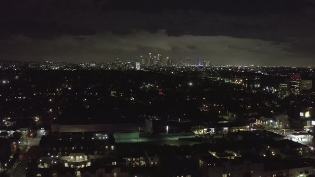 AERIAL: Over Dark Hollywood Los Angeles at Night with Clouds over Downtown and City Lights 