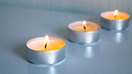 Fototapeta na wymiar Three small burning candles on a light background. Focus on the first candle. Comfort, homely romantic atmosphere. Aroma candles. Postcard, poster.