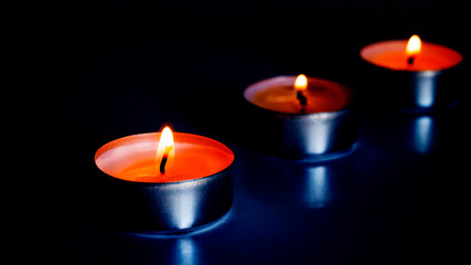Three small burning candles against a dark background. Focus on the first candle. Comfort, homely romantic atmosphere. Aroma candles. Postcard, poster.