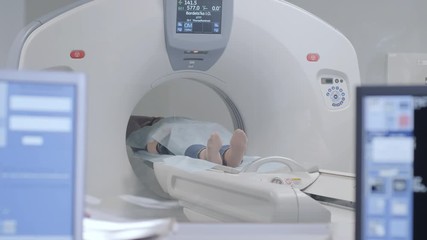 Woman lying on the CT or MRI scanner during machine imaging her body, lights up infrared rays and female patient passes through the circle, crane shot from down to up, room interior, active scene. - Powered by Adobe