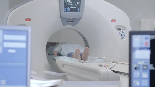 Woman lying on the CT or MRI scanner during machine imaging her body, lights up infrared rays and female patient passes through the circle, crane shot from down to up, room interior, active scene.