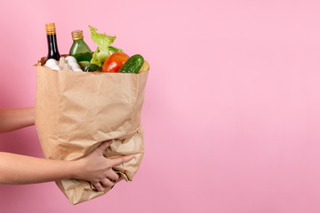 Delivery of food packages. Hands holding a bag of groceries on a pink background