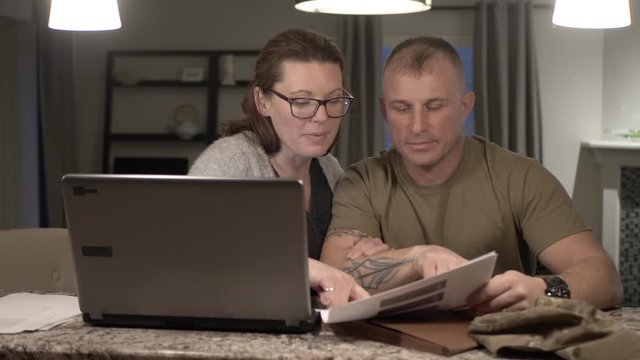 Military Couple Discussing Paperwork At Laptop