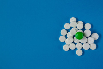 heap of white pills and one green, on a blue background