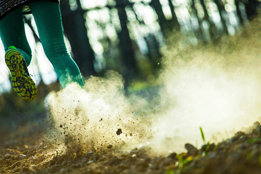 young active womans runner legs jogging running in the forest at sunny off road dust cloud track sport training healthy life style concept