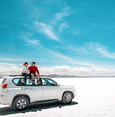 Pair of tourists sitting on white car in Salar de Uyuni